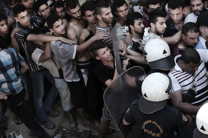 A policeman (2nd-R) pushes a migrant as hundreds wait to complete a registration procedure by the police at a stadium on the Greek island of Kos on August 12, 2015. Tensions on the tourist island are high with its mayor claiming there were 7,000 migrants stranded on Kos, which has a population of only 30,000 people. A Kos police officer was suspended on August 10 after being filmed slapping and shoving migrants queueing outside the local police station as they waited to be documented so they could go on to Athens. The UN refugee agency's division for Europe said 124,000 refugees and migrants have landed in Greece since the beginning of the year. AFP PHOTO / ANGELOS TZORTZINIS (Photo credit should read ANGELOS TZORTZINIS/AFP/Getty Images)
